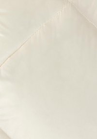 Tejido beige acolchado con una textura suave, que presenta patrones de costura diagonal, creando una apariencia suave y acolchada.