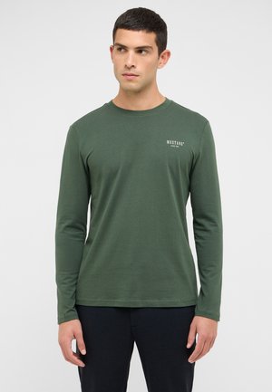 Maglietta a maniche lunghe verde in misto cotone. Presenta scollo tondo e piccolo logo bianco "MUSTANG" sul petto. Tessuto liscio, taglio aderente.