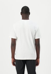 Hvid bomulds t-shirt med korte ærmer og lige snit, med et lille logo mærke på den nederste del. Glat tekstur, minimalistisk design.