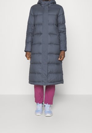 Abrigo acolchado en gris oscuro con capucha, que presenta un corte recto, diseño acolchado y un dobladillo que llega a la mitad de la pantorrilla. Combinado con pantalones rosas y zapatillas.