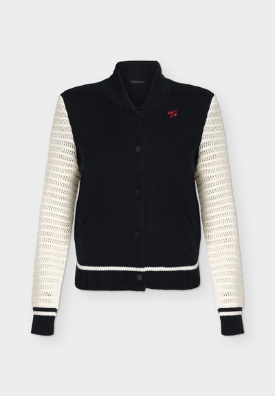 Veste bomber noire en maille avec manches blanches au crochet, poches à l'avant, boutons noirs, col côtelé et petit logo rouge brodé sur la poitrine.
