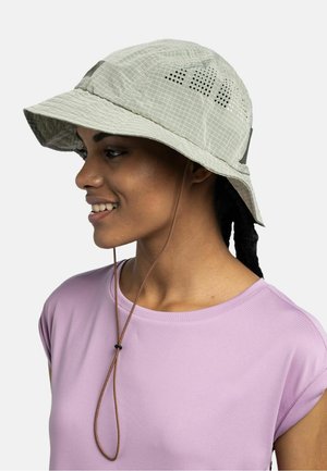 Young woman in a lilac shirt wearing a beige sun hat with ventilation holes and an adjustable chin cord, smiling and looking left.