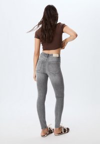 Vaqueros pitillo de talle alto en gris, hechos de mezclilla, con un lavado sutil, dos bolsillos traseros y una etiqueta en la cintura.