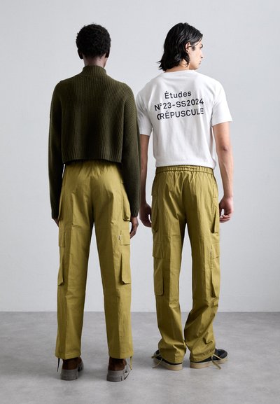 Olive green ribbed cropped sweater and white t-shirt with black text, paired with yellow cargo pants featuring side pockets and an elastic waistband.