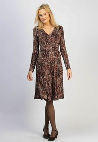 Mekko, jossa pitkät hihat tummassa burgundin värissä ja paisley-kuviointi. V-pääntie, istuva vyötärö, valuva hame, ja paritettu ruskeiden sukkahousujen ja kenkien kanssa.
