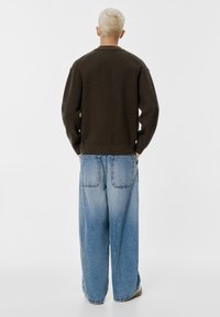 Pulover din tricot cu dungi maro, cu guler rotund, asortat cu blugi din denim cu picioare largi de culoare albastru deschis, având buzunare la spate.