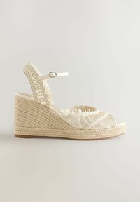 Sandale compensée beige tissée avec bride à la cheville et boucle, avec bout ouvert et design tressé complexe au talon et sur les brides.
