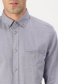 Overhemd met knopen in een gestructureerd marineblauw en wit patroon, met een puntige kraag, een borstzak en bruine knopen.