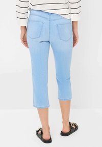 Jean en denim bleu clair, court, avec une coupe droite, doté de deux poches arrière et d'un ourlet. Associé à des sandales noires.
