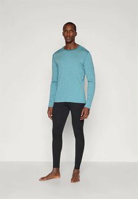 Camisa de mangas compridas azul clara com riscas brancas, combinada com leggings pretas. A camisa tem um decote redondo e um corte descontraído.