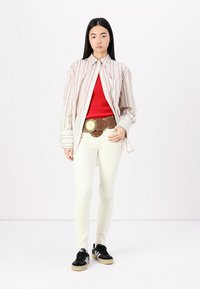 Striped button-up shirt, red tank, white skinny jeans, brown belt with large metal accents, and black sneakers. Smooth fabric and fitted design.