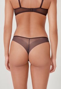 Ensemble de lingerie transparente marron avec une culotte thong, présentant une texture lisse, des bretelles réglables et une couverture minimales à l'arrière.