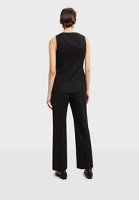 Černý prostřižený outfit obsahující bezrukávovou vestu a široké kalhoty, s jemným proužkovaným vzorem a metalickými akcenty po celé délce.