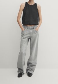 Zwarte mouwloze top met een relaxte pasvorm, gecombineerd met hoog getailleerde lichtgrijze wijde broek. Zwarte platte schoenen maken de outfit compleet.