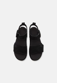 Sandales noires à bout ouvert avec des sangles réglables sur les orteils et les chevilles, dotées de semelles rembourrées douces et d'un logo UGG discret sur les sangles des orteils.