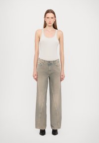 Hellgraue weit geschnittene Jeans mit einem verwaschenen Finish, kombiniert mit einem taillierten weißen Tanktop. Verfügt über Fronttaschen und dezente Steppnähte.