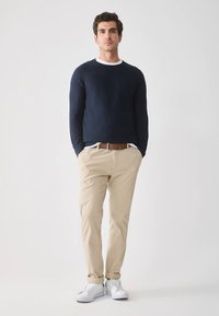 Navy sweater with white collar, beige pants, and white sneakers. The outfit features a brown belt and a casual, fitted design.