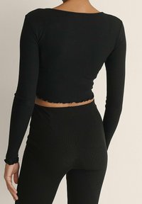 Schwarzes, langärmliges, geripptes Cropped-Top mit gewelltem Saum, figurnaher Passform und weicher Textur, kombiniert mit passenden hochgeschnittenen Hosen.