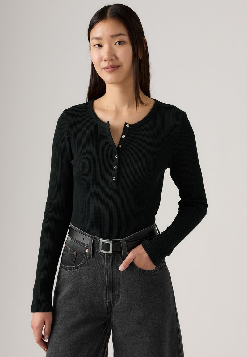 Sort ribbet langærmet top med knapudskæring, parret med højtaljede grå jeans og et sort bælte. Simpelt, tætsiddende design.