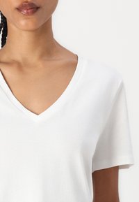 Hvit bomulls T-skjorte med V-hals og korte ermer, med en myk tekstur og minimale sømmer. Ingen mønstre eller detaljer synlige.