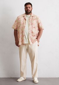 Korte mouwen shirt met een beige basis en een rood bladenpatroon, gecombineerd met lichtcrème broek en witte sneakers, met een relaxte pasvorm.