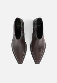 Stivaletti in pelle marrone con punta affusolata, chiusura con cerniera laterale e texture liscia. Suola nera robusta con accenti di design minimi.