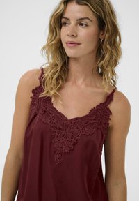 Bordo gornji dio s delikatnim čipkastim detaljima na izrezu, s tankim naramenicama i mekom, laganom teksturom tkanine.