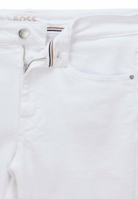 Bílé džínové kalhoty s zipovým zapínáním, knofl íkovým uzávěrem a bočními kapsami. Minimalistický design s jemným švem a pruhovaným detailem uvnitř pásku.