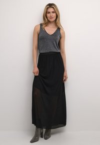 Schwarzer Maxikleid mit einem transparenten Einsatz am unteren Rand kombiniert mit einem grauen ärmellosen Top. Strukturierter Stoff und taillierter Bund. Funkelnde Stiefel.