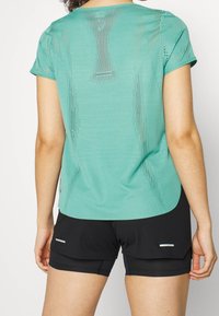 Jasnoniebieska koszulka sportowa z siateczkowymi detalami na plecach, krótkie rękawy i zaokrąglony dół, w połączeniu z czarnymi szortami z odblaskowymi akcentami.