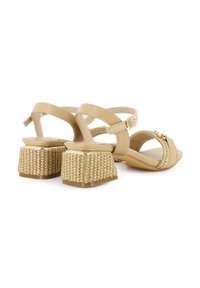 Sandalias beige con una correa brillante y un tacón de bloque texturizado trenzado. Cuenta con una hebilla decorativa y correas en el tobillo ajustables.