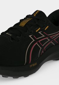 Μαύρο παπούτσι για τρέξιμο ASICS με ροζ και άσπρες πλαϊνές ρίγες, κίτρινες θηλιές κορδονιών, σόλα FF Blast και ετικέτα Gore-Tex κοντά στη μύτη.