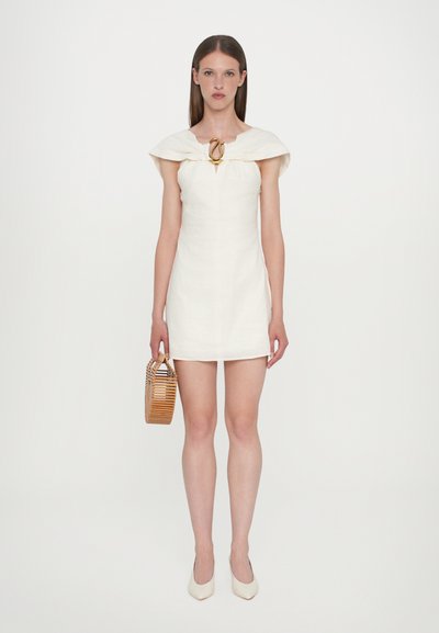 White linen dress with a fitted silhouette, featuring a wide collar and gold-tone hardware at the neckline. Model holds a woven basket bag.