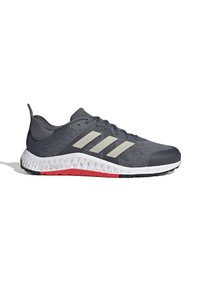 Gray athletic shoe with three silver stripes, textured upper, lightweight design, and a white and red rubber sole with a zigzag pattern.