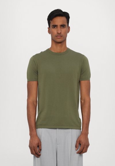T-shirt à manches courtes vert olive fabriqué en tissu léger. Présente un col rond et une silhouette ajustée.