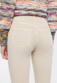 Jeans ajustados beige con bolsillos traseros, con una textura suave y detalles de costura sutiles, combinados con un suéter de punto multicolor.