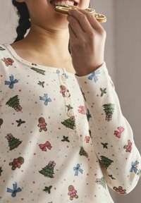 Langärmliges, hellcremefarbenes Oberteil mit festlichen Motiven von Lebkuchen, Weihnachtsbäumen und Schleifen. Verfügt über eine gerippte Textur und Knöpfe am Ausschnitt.
