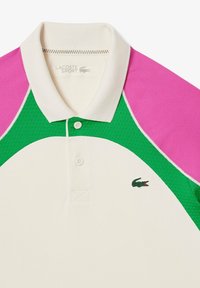 Pikétröja med en färgblockdesign i grönt och rosa, med en texturerad tygkvalitet, kontrasterande vit krage och logotyp på vänster sida.