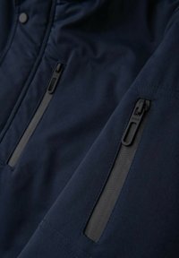 Veste bleu marine avec finition mate élégante ; comprend deux poches zippées et des détails de couture, offrant un design moderne et fonctionnel.