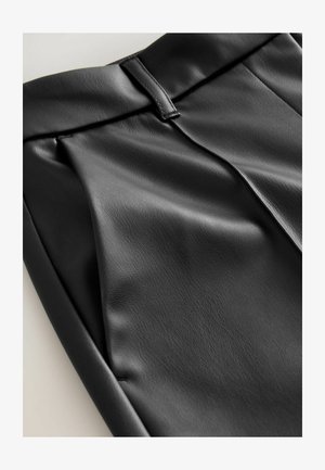 Melni mākslīgas ādas bikses ar gludu tekstūru, kurām ir plakans jostasvīrs, krokas un diskrēta aizmugures vīle.