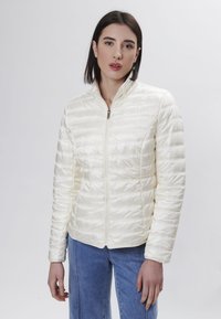 Giacca trapuntata avorio con chiusura a zip, colletto alto e maniche lunghe. Realizzata in tessuto leggero e lucido. Design semplice senza motivi visibili.