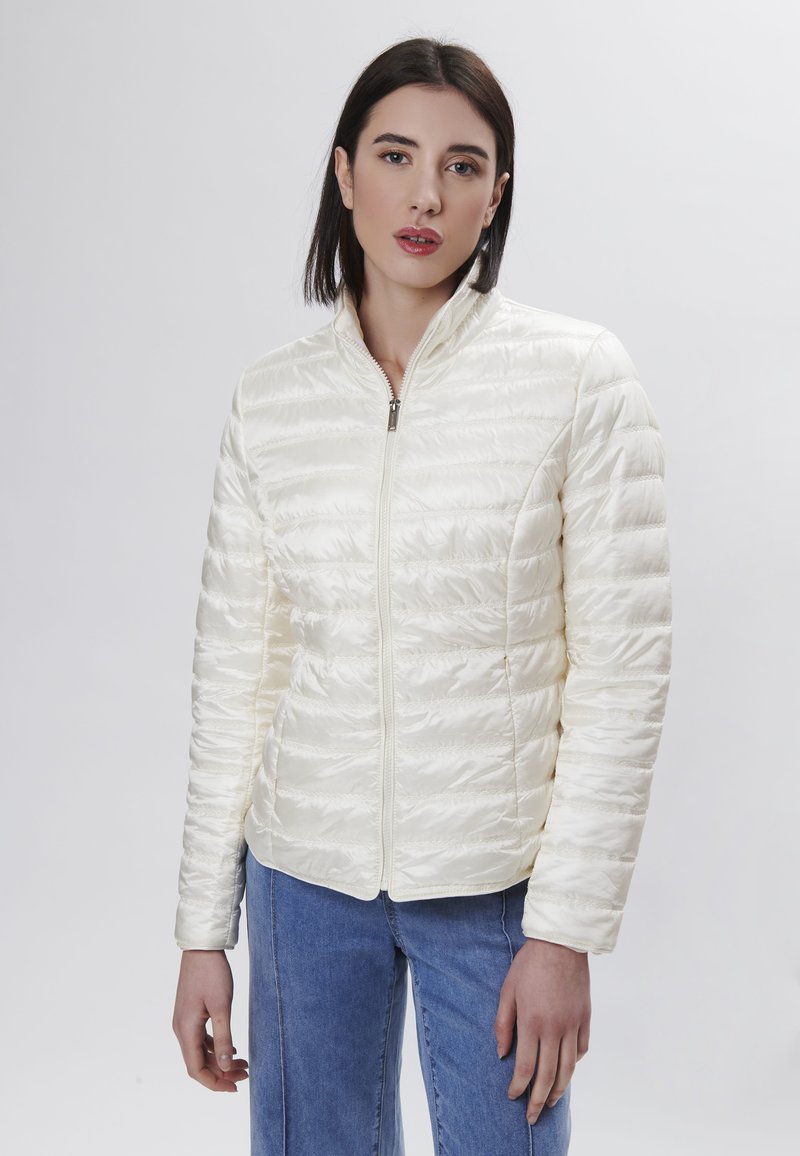 Giacca trapuntata avorio con chiusura a zip, colletto alto e maniche lunghe. Realizzata in tessuto leggero e lucido. Design semplice senza motivi visibili.