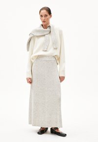 Witte gebreide trui gecombineerd met een geribbelde, enkel-lange, lichtgrijze rok met gespikkelde textuur. Zwarte schoenen met zilveren accenten.