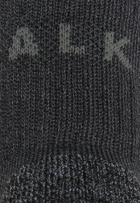 Calcetín negro de punto que presenta un patrón texturizado con una sutil marca en letras grises en contraste. El material parece suave y flexible.
