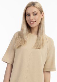 Beige tröja med rund hals och korta ärmar i en avslappnad passform. Har en strukturerad yta och diskret söm detaljer längs fram.