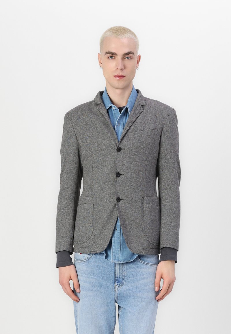 Grau blazer aus einem strukturierten Stoff mit einem Ein-Knopf-Verschluss, Reverskragen und zwei Vorderaschen, über einem Denimhemd getragen.