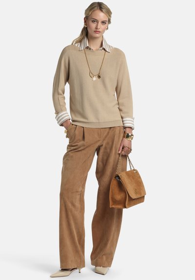 Pull en tricot beige, pantalon large en daim marron clair et talons beiges. Les accessoires comprennent un collier, des bracelets et un sac à main marron avec des accents dorés.