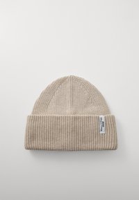 Beež neelatud beanie, millel on soonikuline tekstuur, volditud ääre ja väike brändi silt küljel. Lame ülaosa disain.