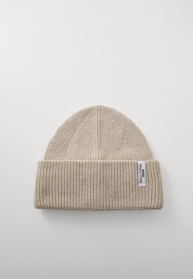 Beež neelatud beanie, millel on soonikuline tekstuur, volditud ääre ja väike brändi silt küljel. Lame ülaosa disain.