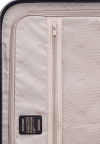 Harde koffer interieur met beige stof en een subtiel logo patroon, netvak en dubbele ritsen voor organisatie.